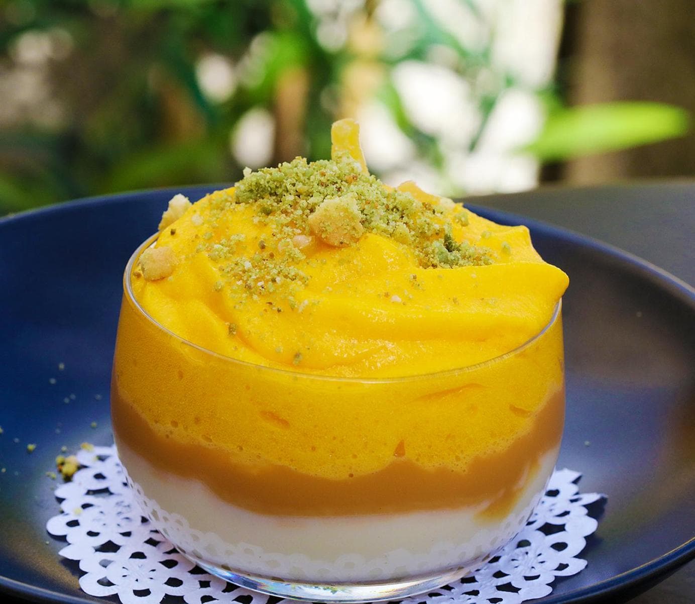 A layered dessert cup with white cream, caramel, and yellow mousse dusted with crushed nuts.