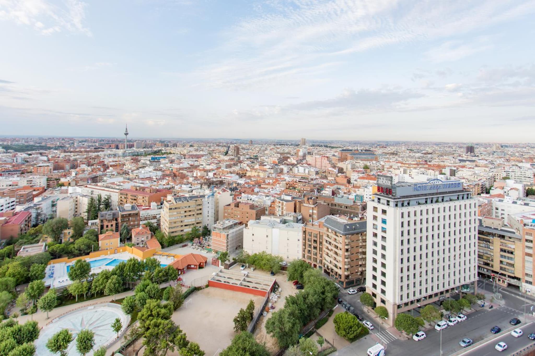 Panoramic elevated view over city rooftops, showing surrounding streets, residential blocks, and a green park.