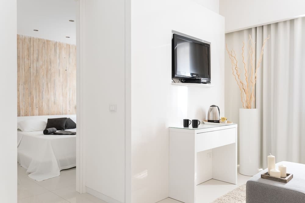 Modern white living area with a wall-mounted television and doorway into a wood-paneled bedroom.