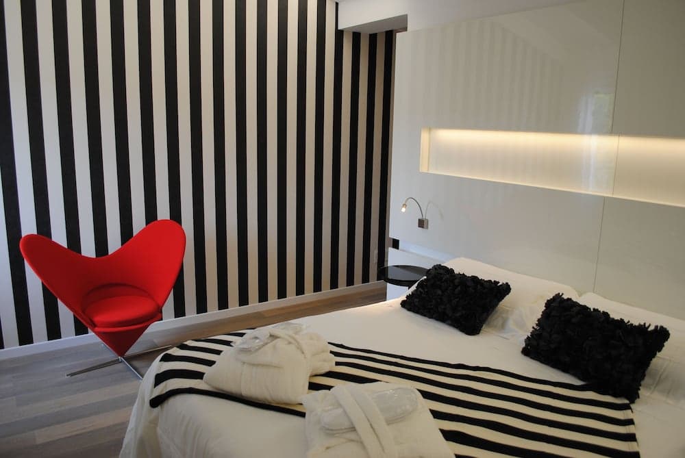 Bedroom with vertical black-and-white striped wallpaper, a red accent chair, and a bed.