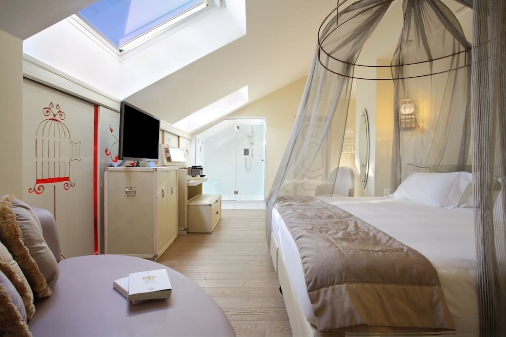 An attic bedroom with a skylight, a draped canopy bed, wooden floors, and an en-suite glass shower.