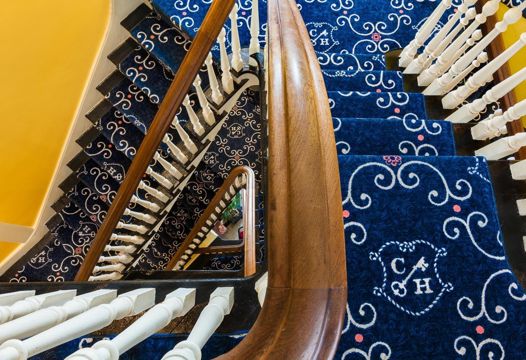 A high-angle view down a winding wooden staircase covered in patterned blue carpeting.