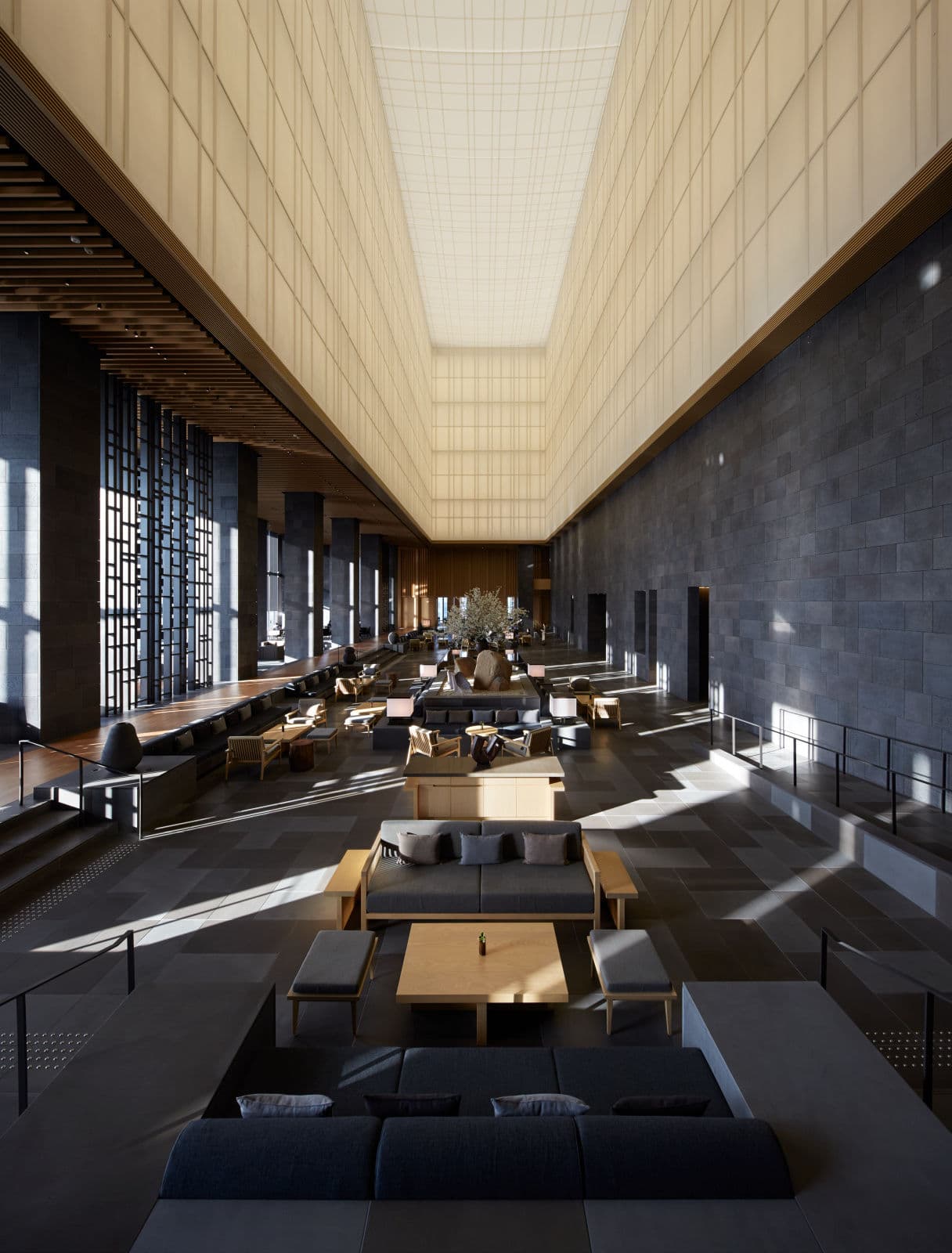 A cavernous hotel lobby with a soaring paper lantern ceiling, dark stone walls, and low lounge seating in sunlight.