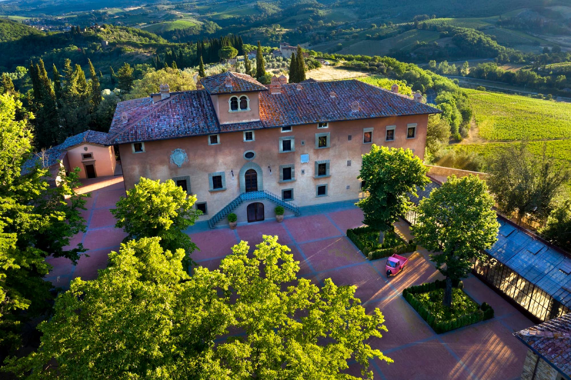 Aerial view of the Vignamaggio villa and terracotta courtyard surrounded by green trees and Tuscan hills.