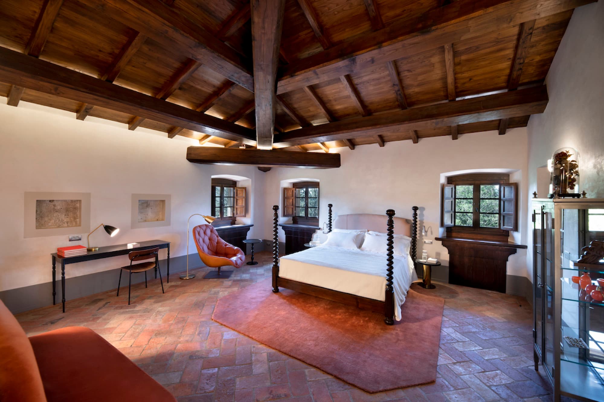A bedroom with exposed timber ceiling beams, terracotta tile flooring, and a carved wooden poster bed.