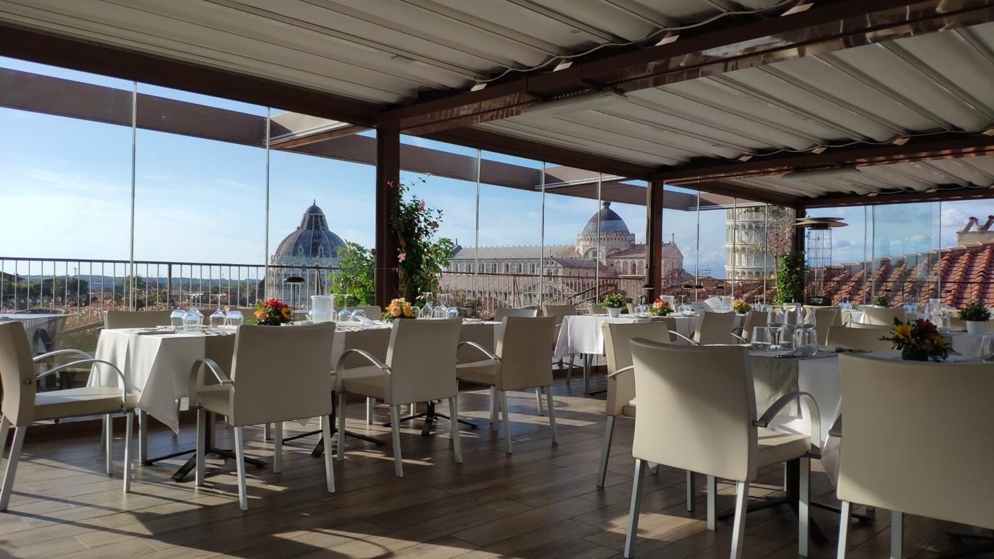 A glass-enclosed dining terrace overlooking the dome of Pisa Cathedral and the Leaning Tower.