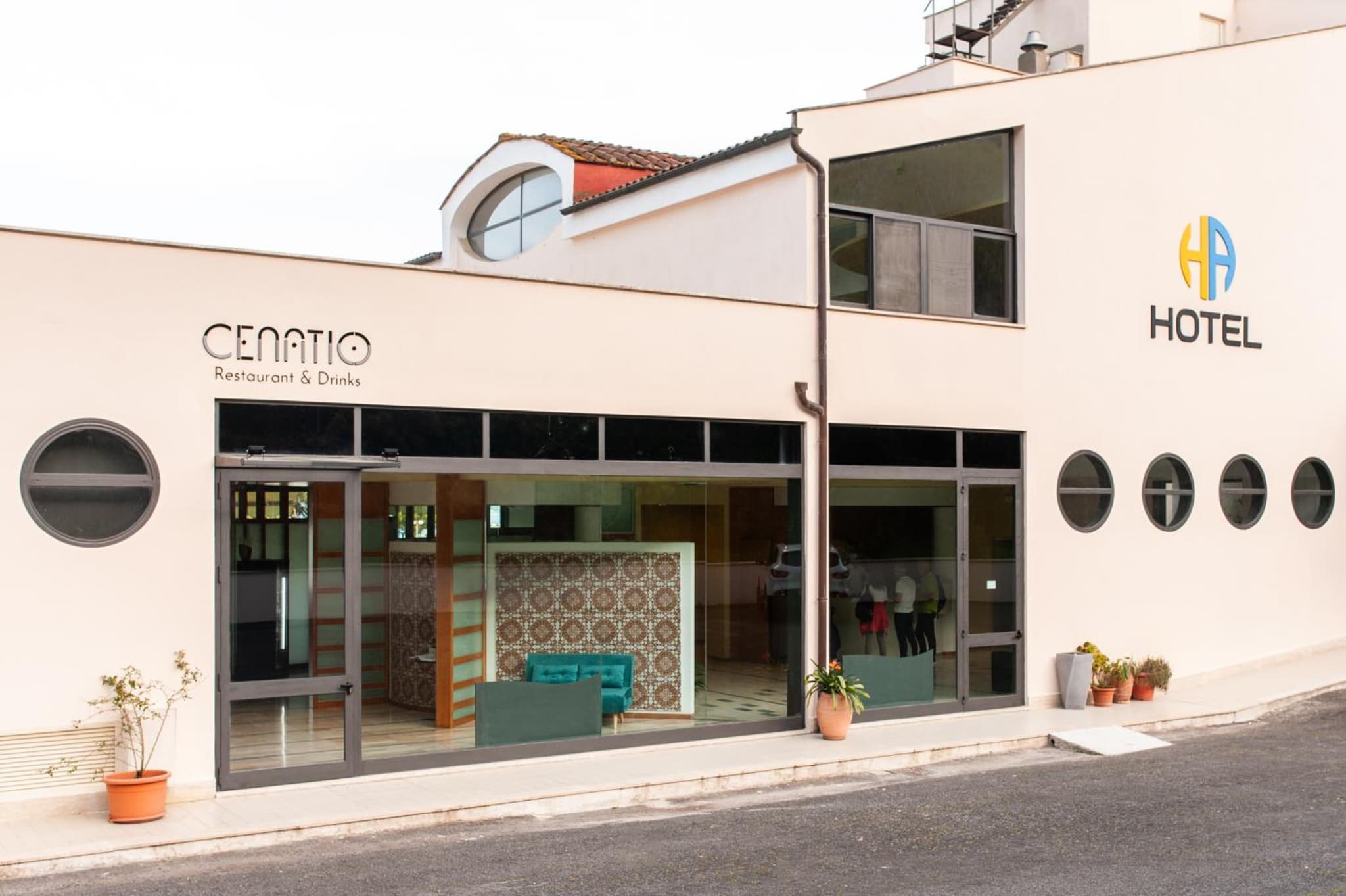 The exterior facade of Cenatio restaurant with wide glass windows, round porthole openings, and potted plants.