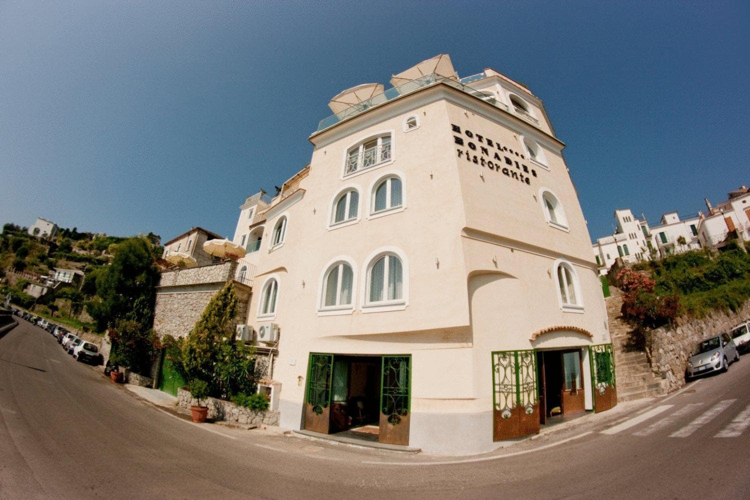A wide-angle street view of the cream-colored hotel building along a curved mountain road.