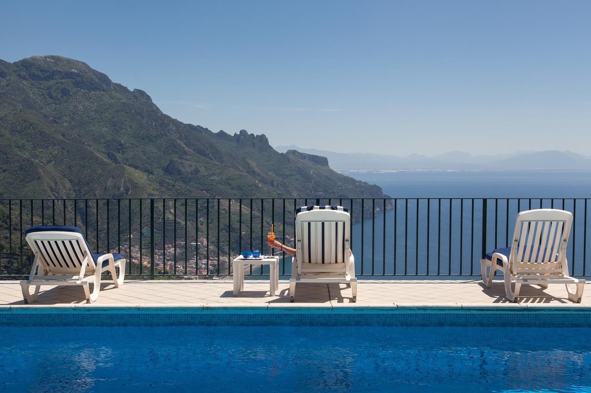 Lounge chairs line the edge of a swimming pool with a view of the sea and coastal cliffs.