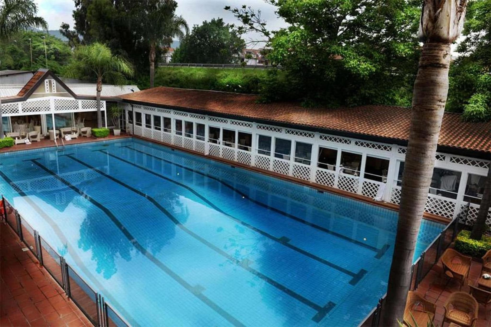 An elevated view of the rectangular swimming pool flanked by a red-tiled pavilion and palm trees.