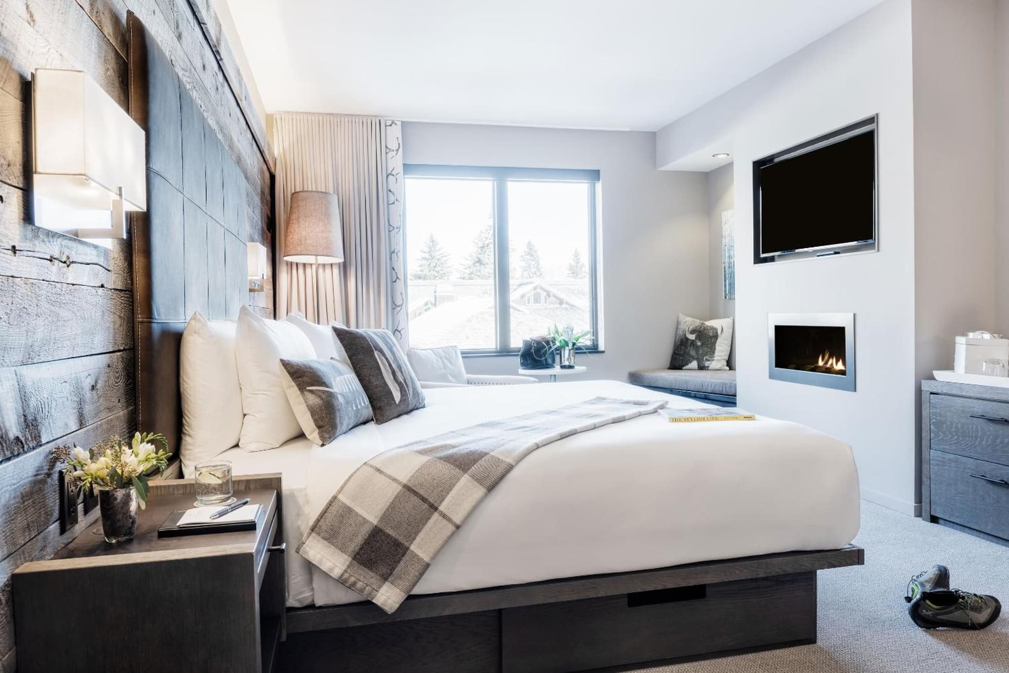 A bedroom featuring a bed against a weathered wood wall, an in-wall fireplace below a TV, and a window.