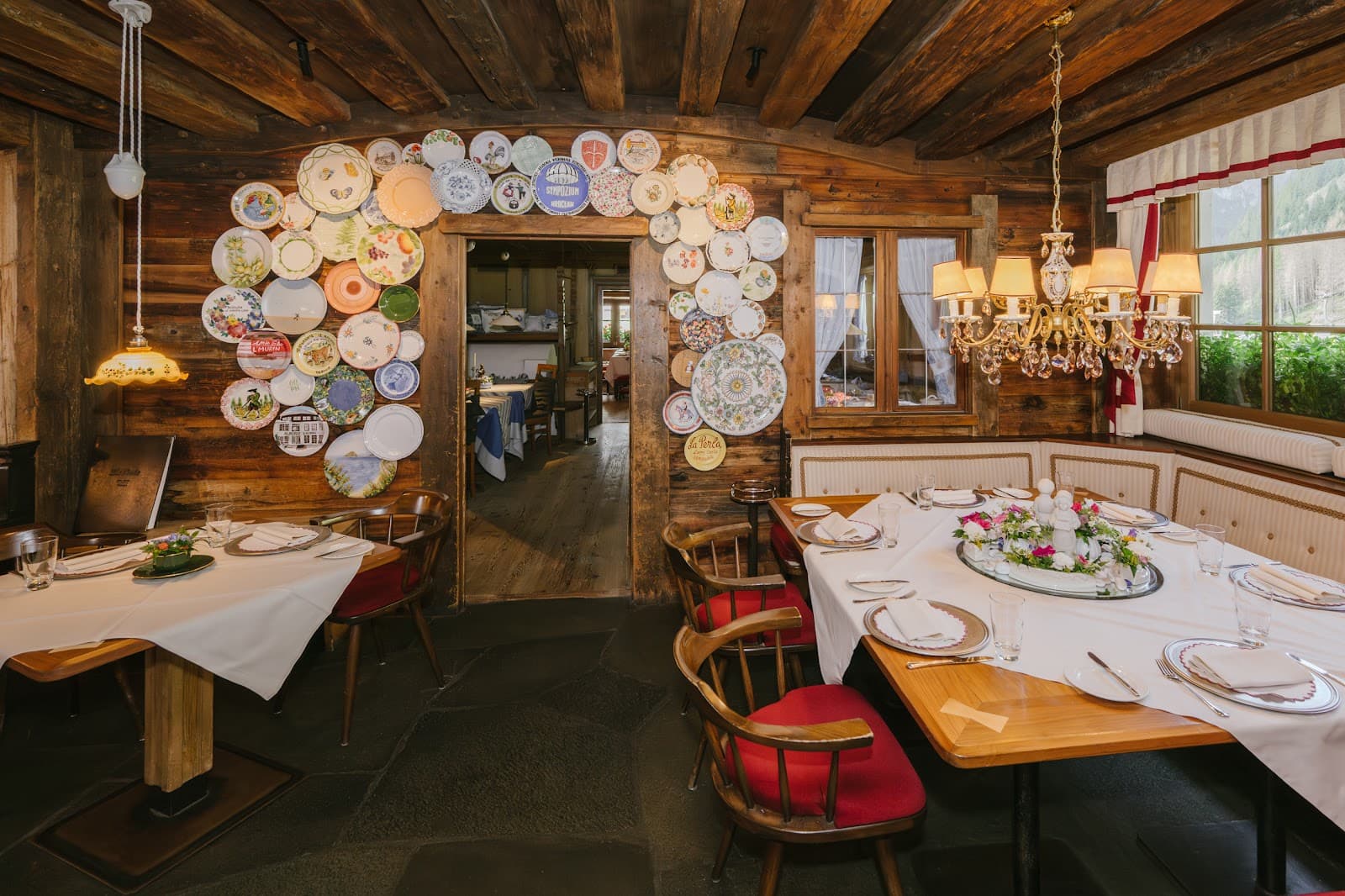 Rustic dining room with dark timber walls and ceiling, set tables with white linen, and decorative plates around a doorway.