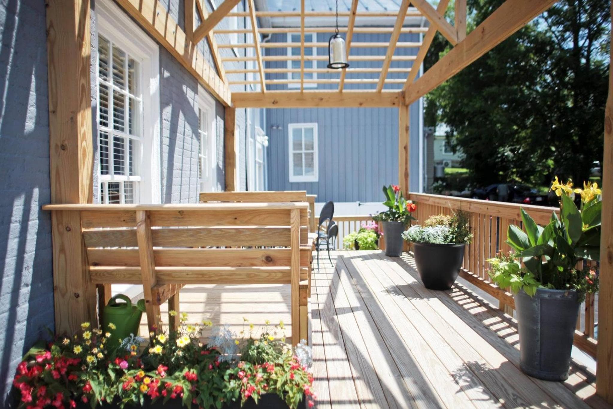 Sunlight filters through a timber pergola onto a wooden deck lined with benches and potted plants.