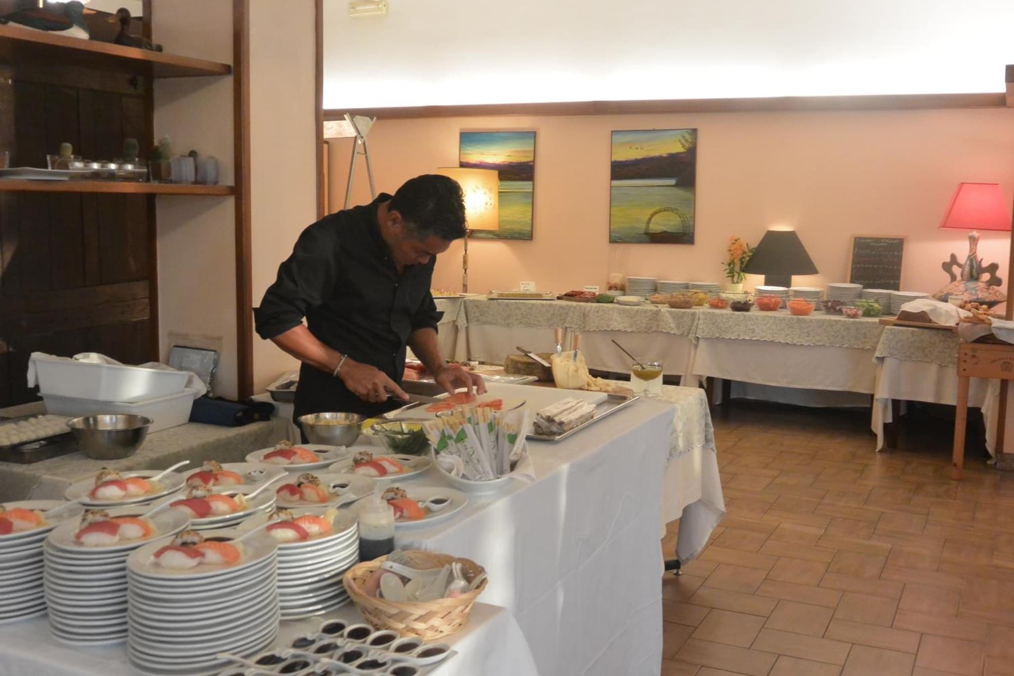 Chef slices fish at a buffet table laden with plates of prepared sushi and food displays.