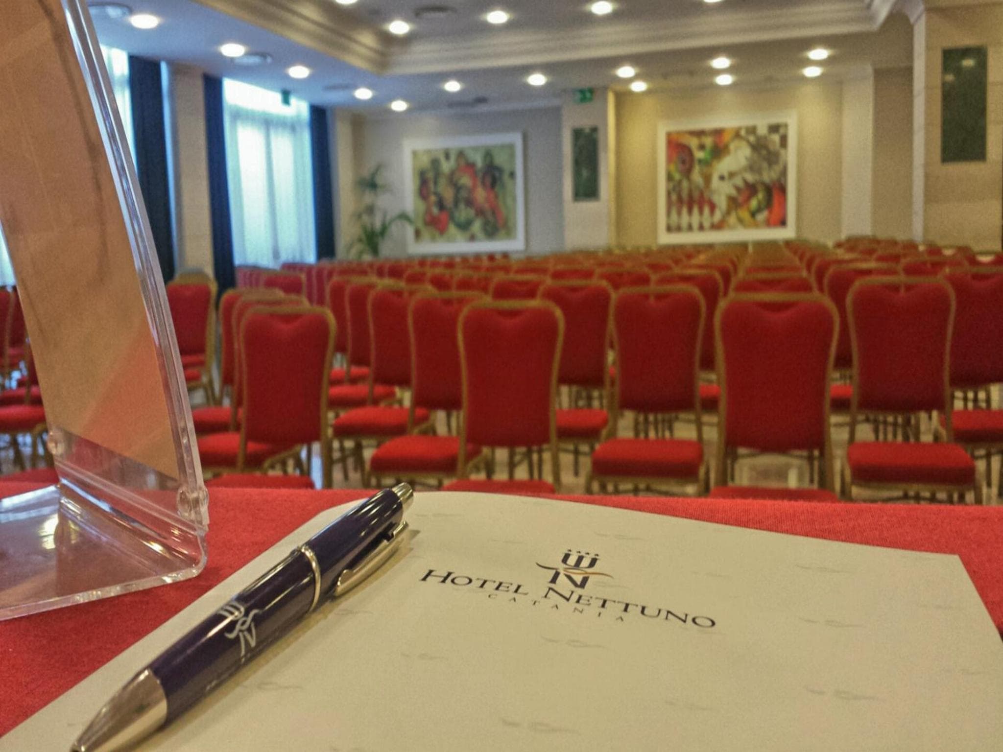 A branded notepad and pen resting on a table in front of rows of red chairs in a conference hall.