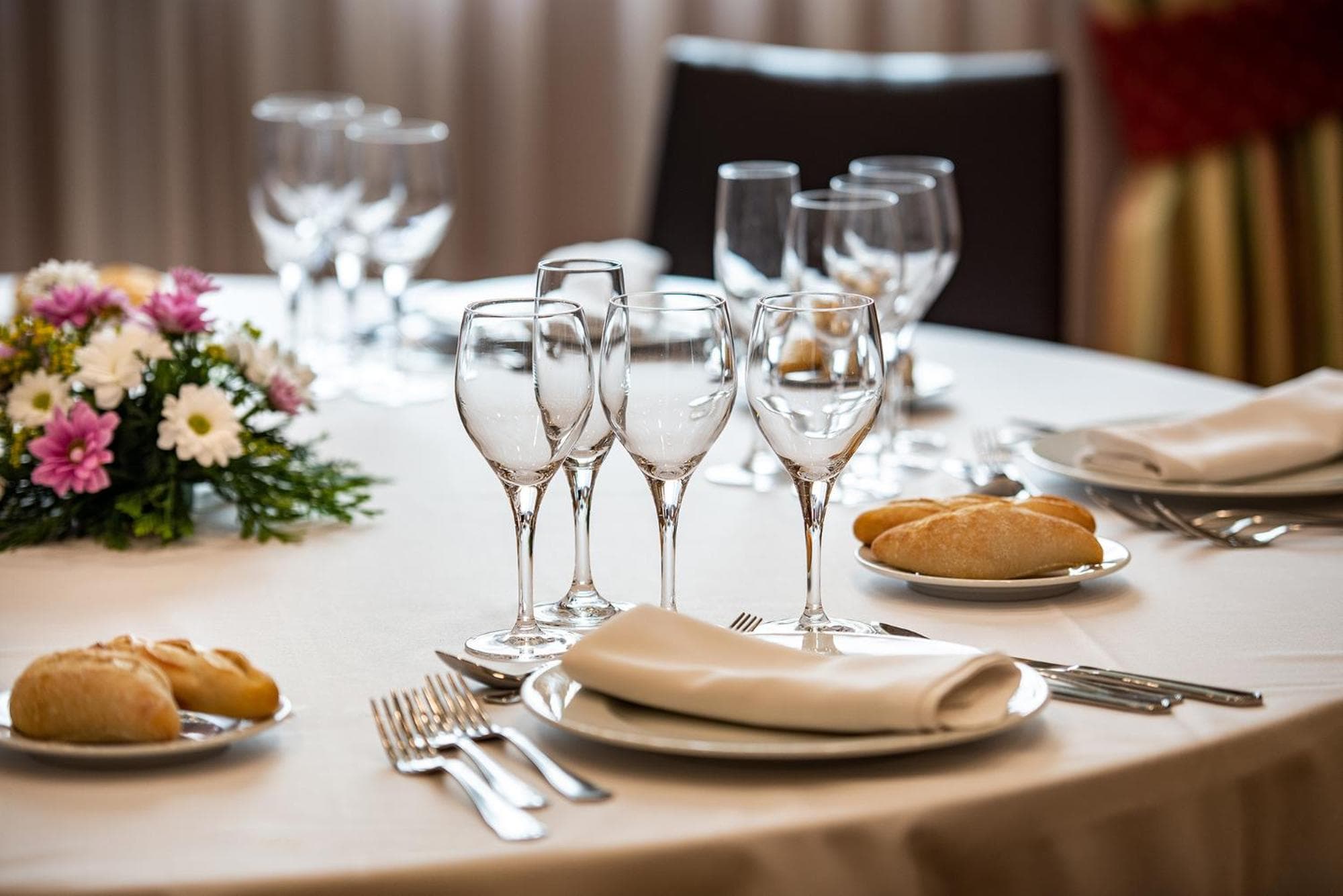 A round banquet table set with white linens, wine glasses, bread plates, and a floral centerpiece.