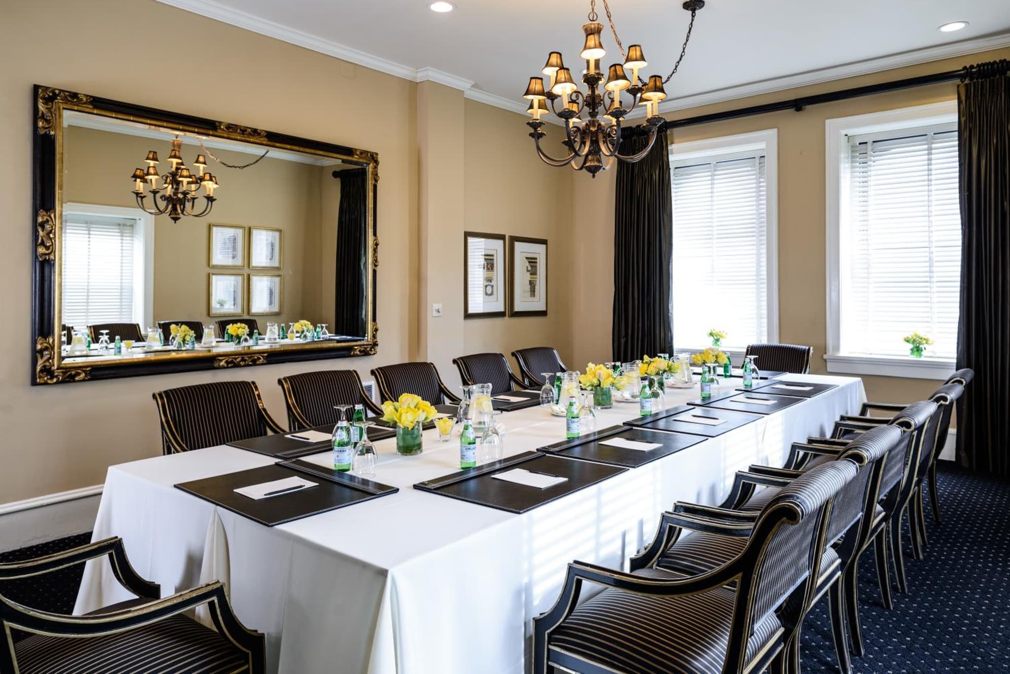 A meeting room table draped in white cloth, flanked by striped armchairs below a chandelier and framed mirror.