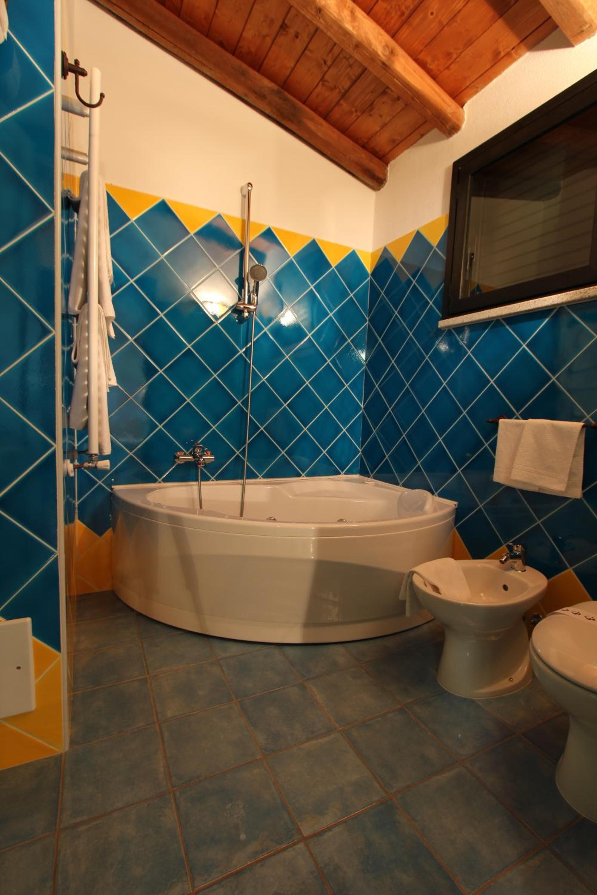 Bathroom with blue and yellow wall tiles, a corner soaking tub, and an exposed wooden beam ceiling.