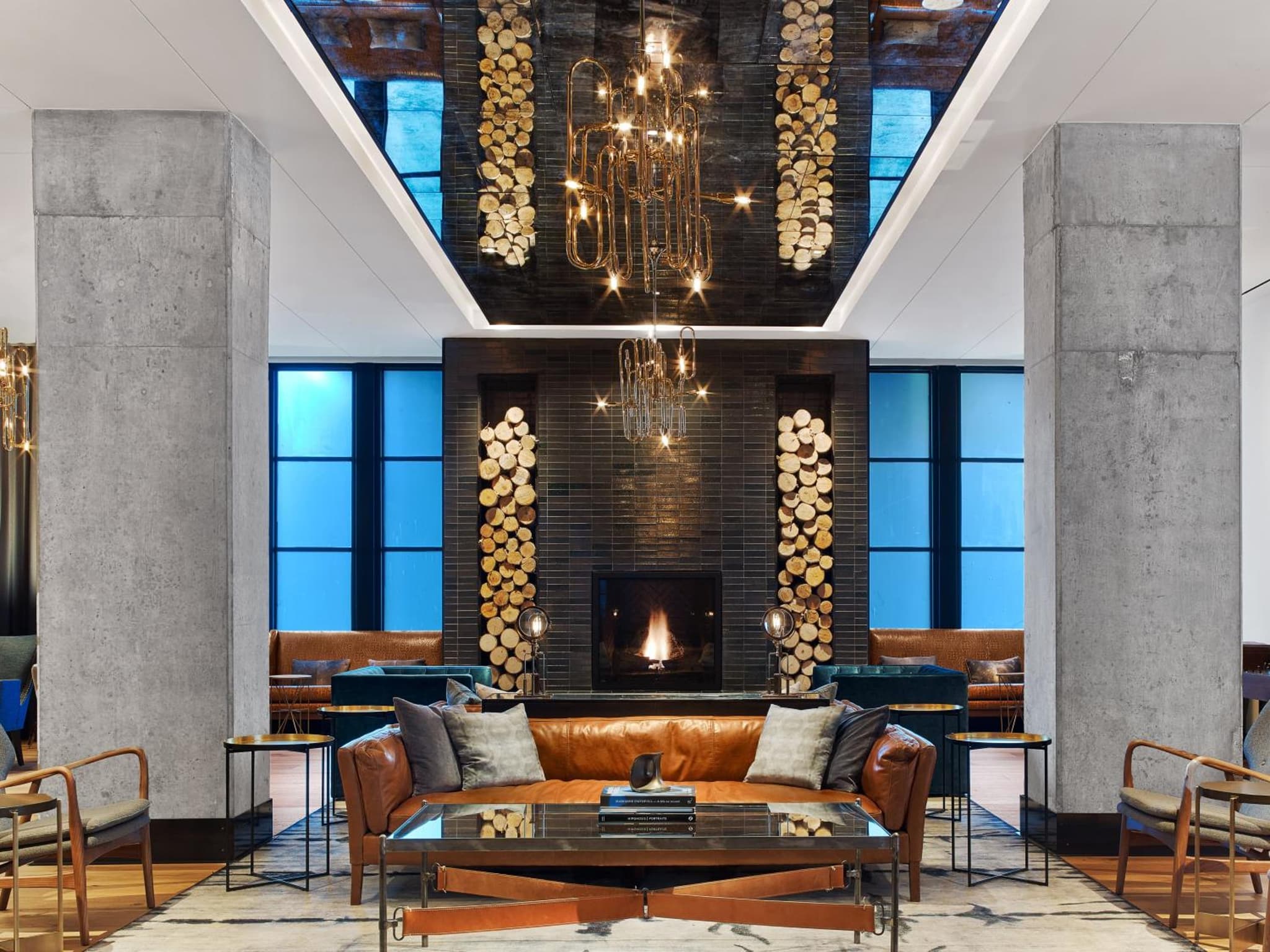 A lounge with a leather sofa, glass coffee table, and fireplace flanked by tall niches of stacked firewood.