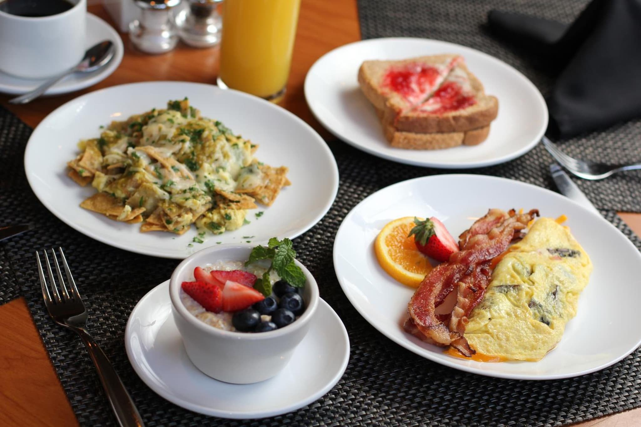 A breakfast spread of chilaquiles, an omelet with bacon, jam-topped toast, and oatmeal with fresh berries.