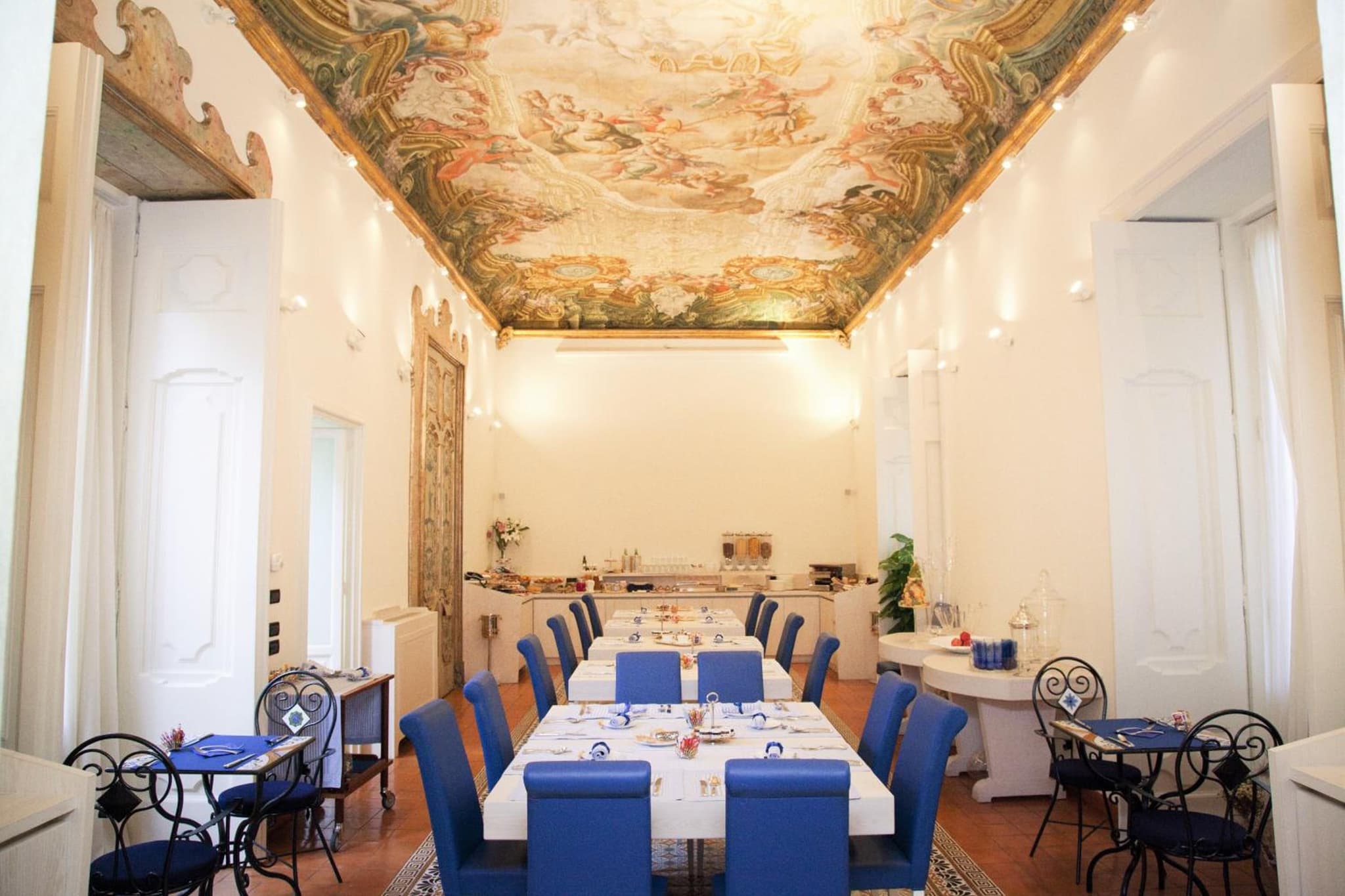 Maison Tofani dining room featuring tables with blue chairs under an ornate frescoed ceiling.