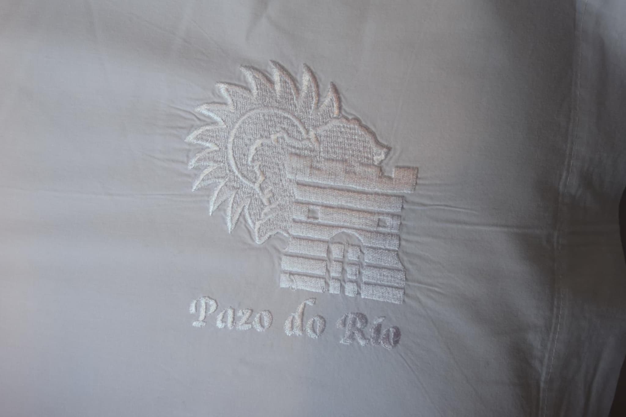 White fabric embroidered with a fortress crest and Galician lettering.