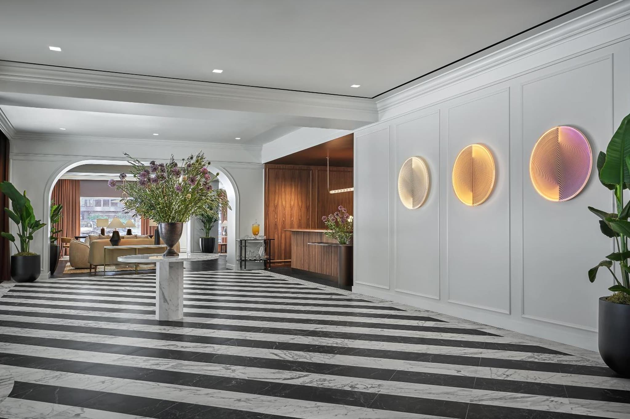 Lobby with diagonal striped marble floors, a tall floral arrangement, and illuminated circular wall sculptures.