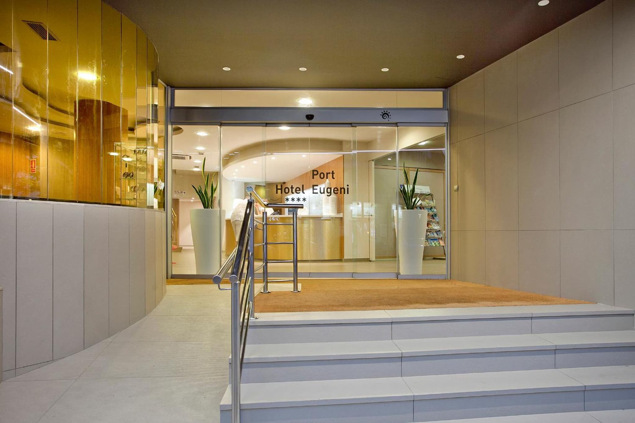 Tiled steps with metal handrails leading to glass sliding entrance doors opening onto a reception area.