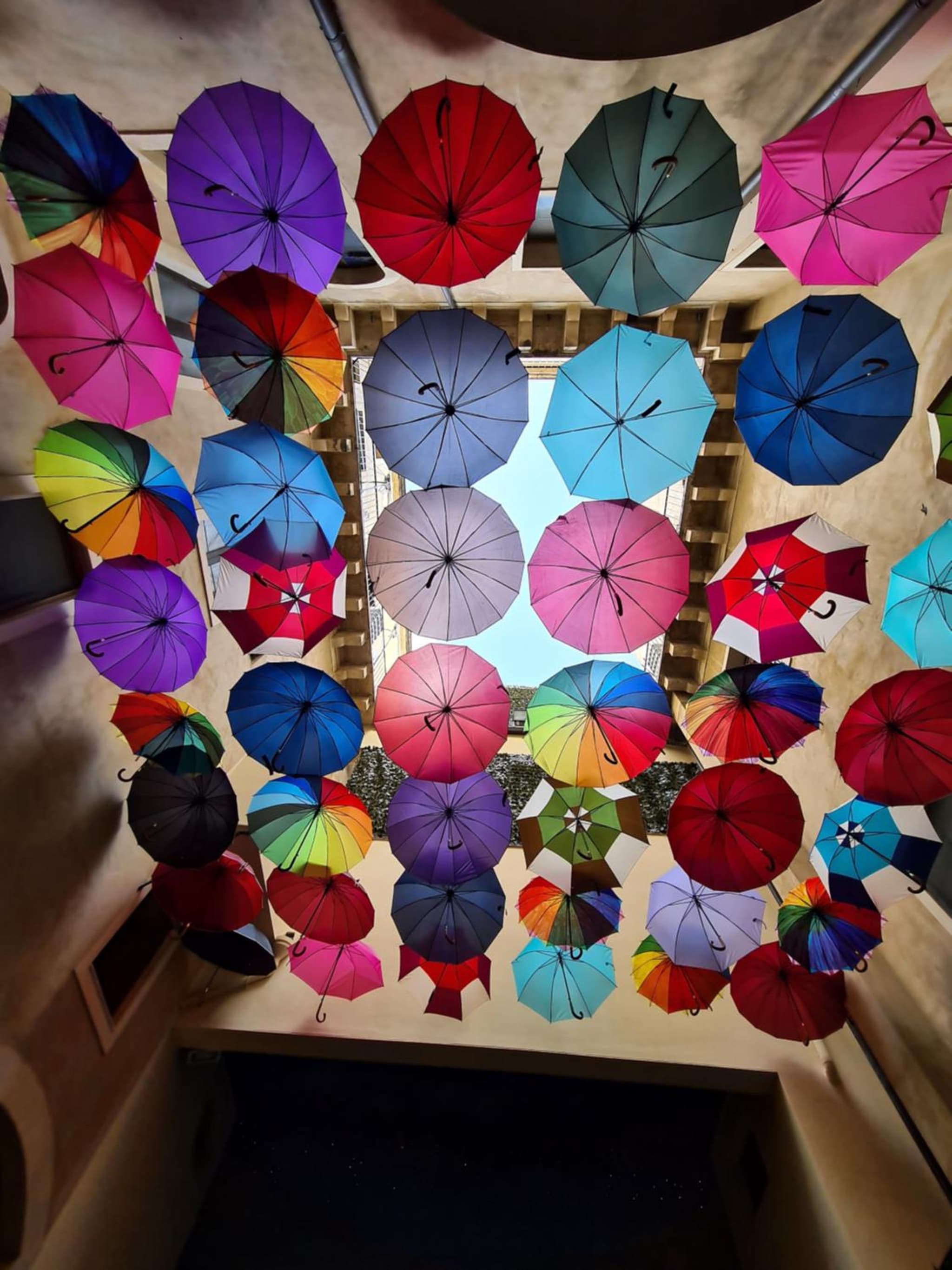 Looking up at an open-air courtyard canopy filled with colorful umbrellas suspended beneath the sky.