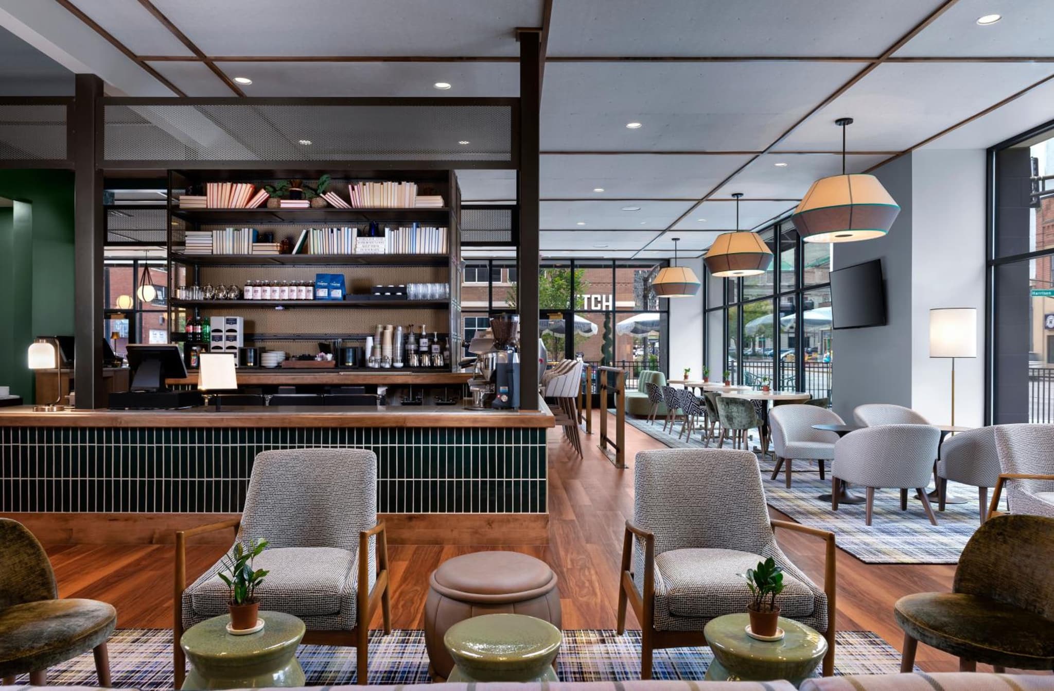 Lounge and bar area with tiled counter, mid-century modern chairs, low tables, and large street-facing windows.