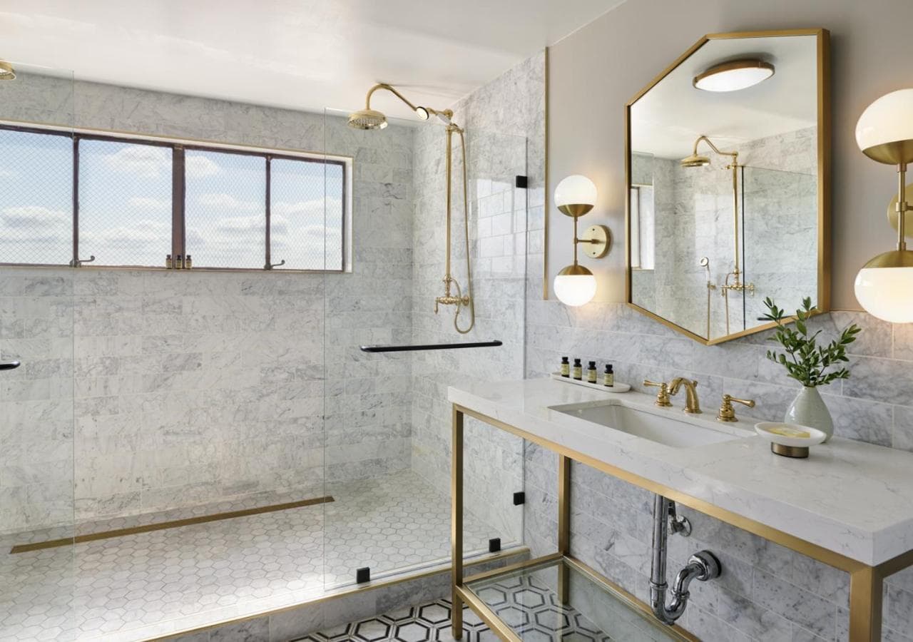 Marble bathroom with a glass-enclosed shower, brass fixtures, hexagon floor tiles, and a vanity counter.