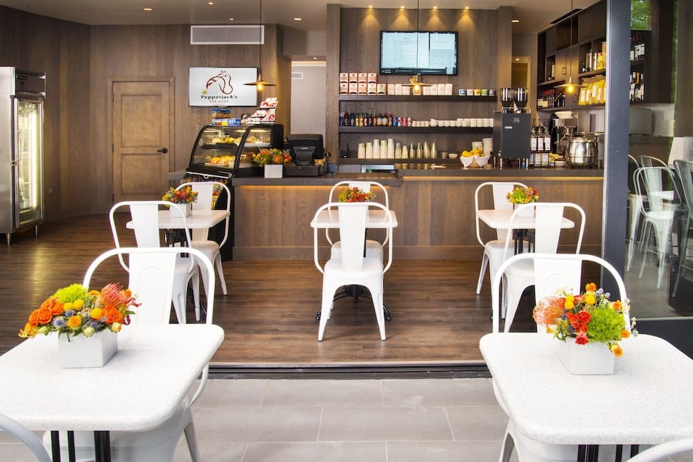 Cafe interior with small tables, white chairs, floral arrangements, and a wood-paneled service counter.