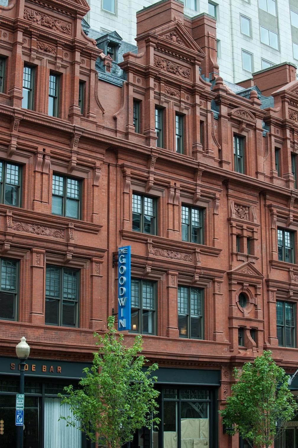 Detailed view of the red terracotta brick facade with decorative window surrounds and a blue vertical sign.