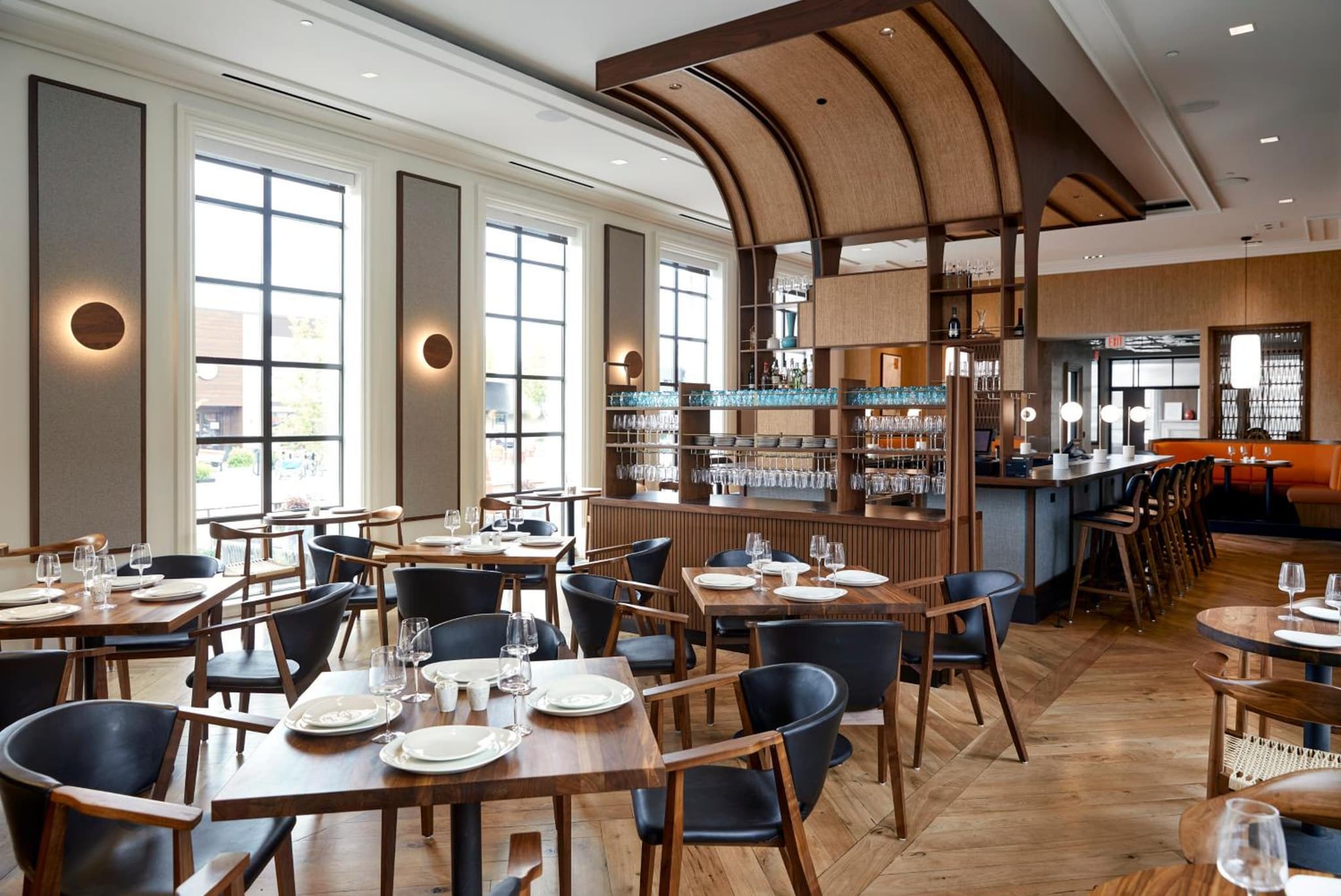 Restaurant dining area with wooden tables, dark leather chairs, tall grid windows, and an arched timber canopy.