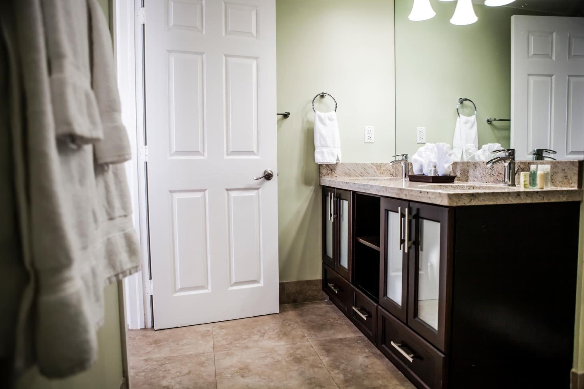 Bathroom with a dark wood vanity, stone countertop, sinks, and an open white door.