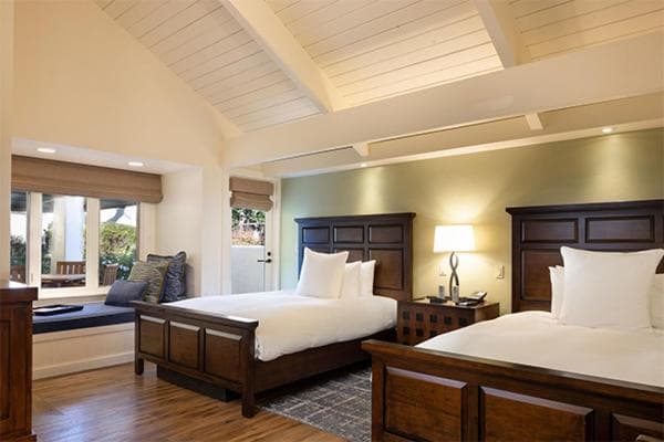 A guest room at The Quail with dark wood beds, vaulted beamed ceilings, and a built-in window seat.