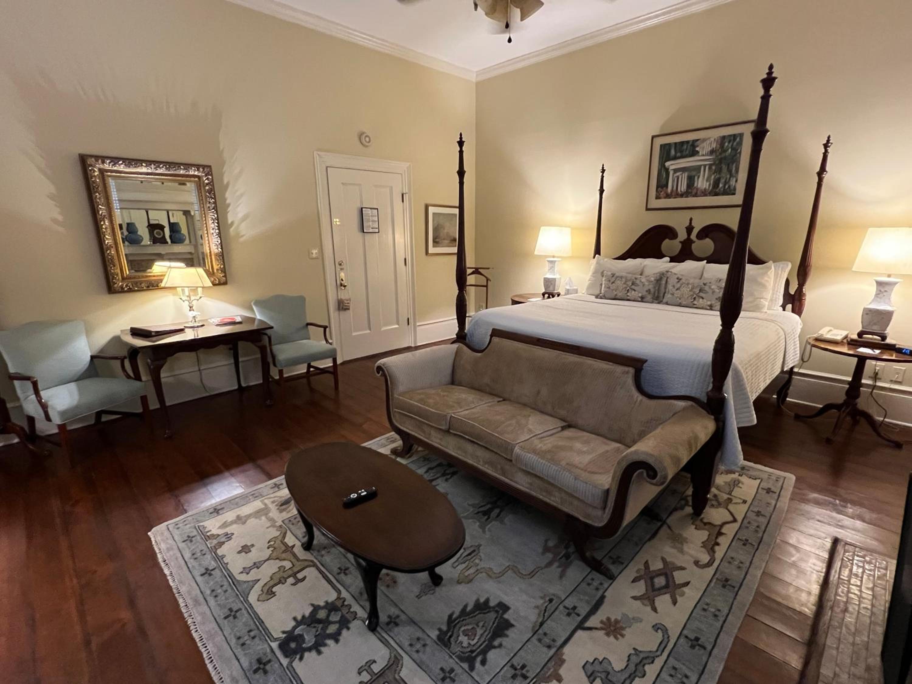 Guest room with a wooden bed, patterned rug, settee, oval coffee table, and an ornate gilded mirror.