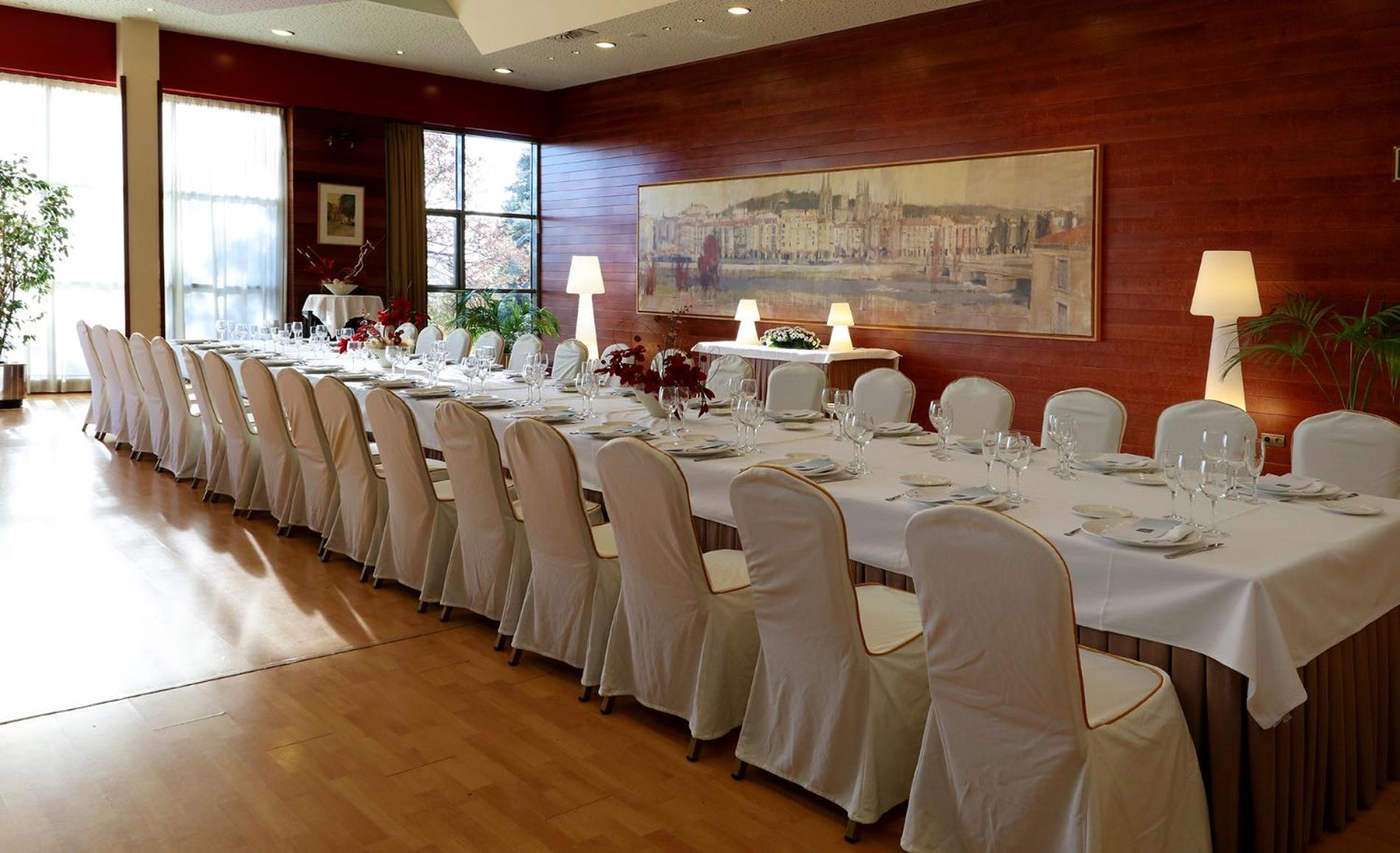 A long dining table draped in white linens alongside wood-paneled walls and a panoramic cityscape painting.