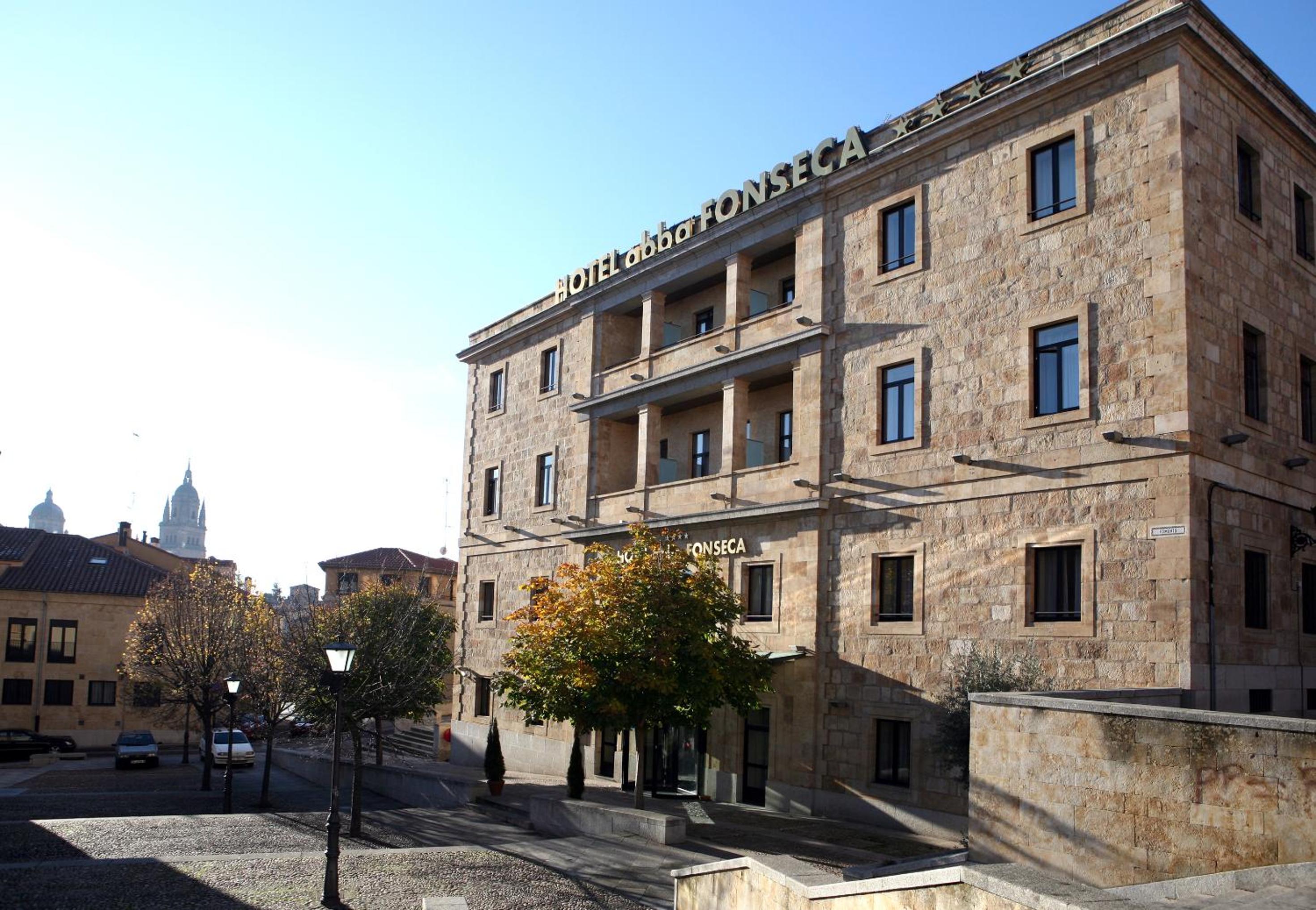 The stone facade of Hotel abba Fonseca under a clear sky, facing a cobblestone square.