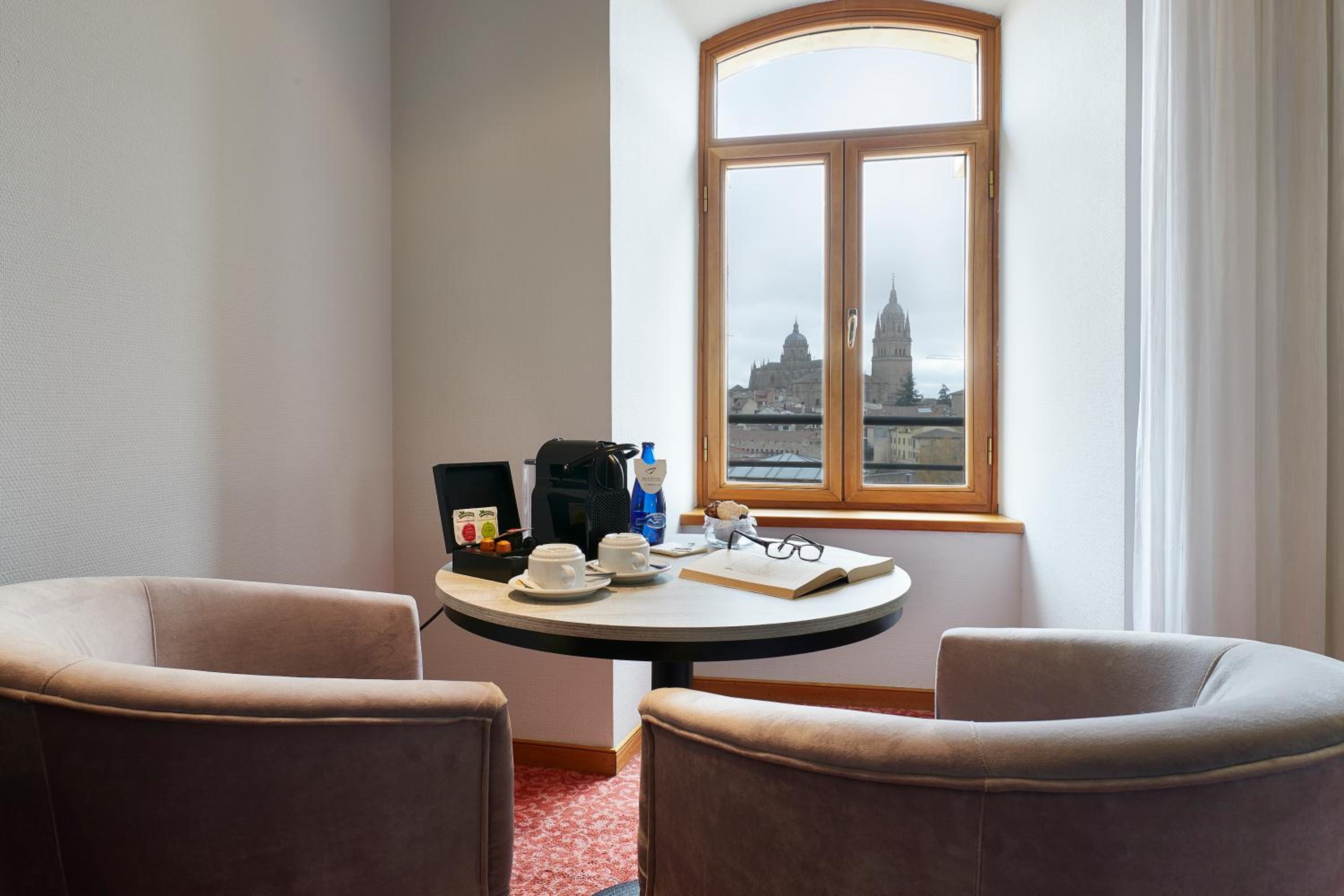 Armchairs around a small table next to a window framing distant cathedral towers.