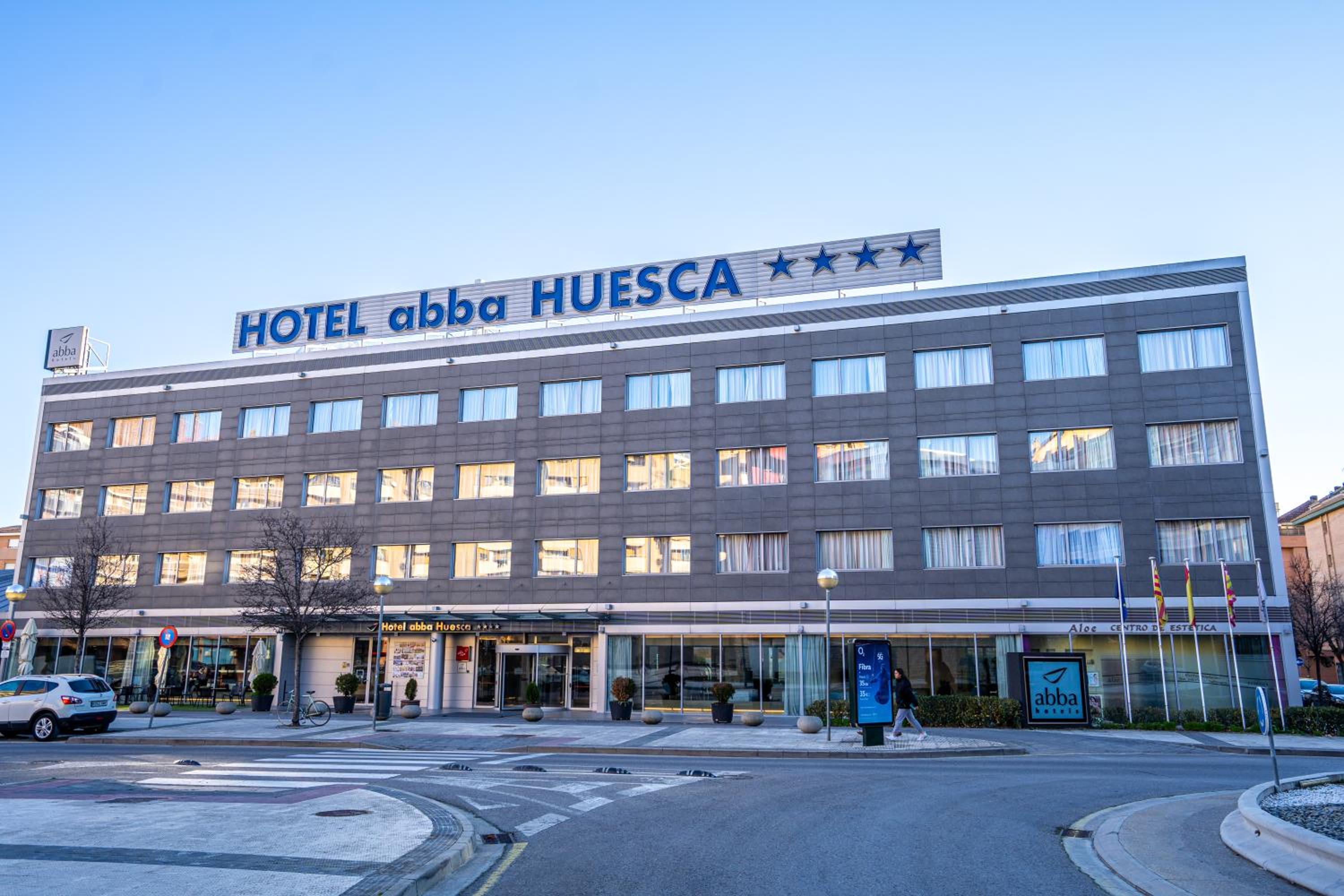 Modern exterior hotel facade across an asphalt road, featuring grey siding and wide rows of windows in daylight.