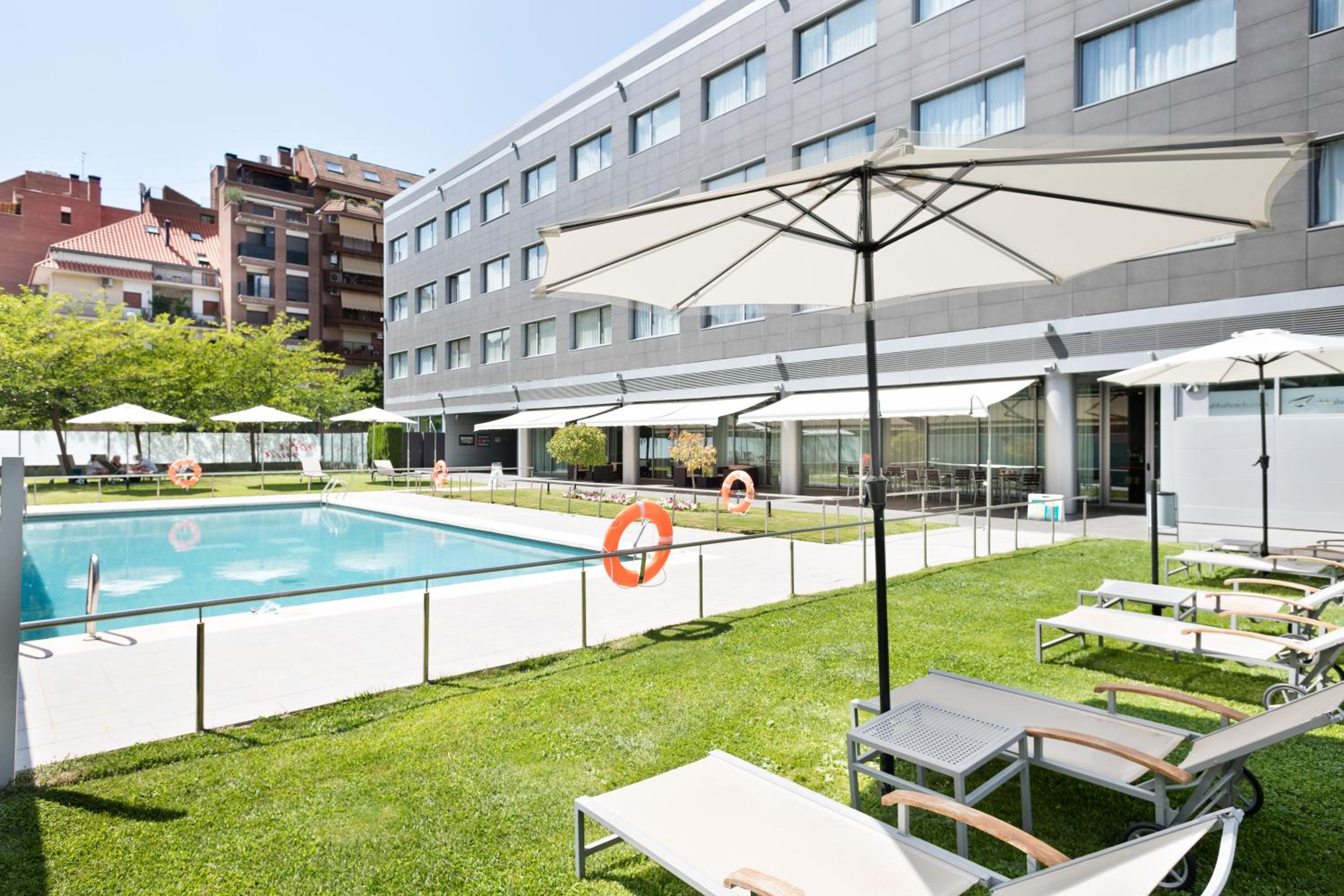 Outdoor swimming pool bordered by a green lawn with sun loungers and white parasols in bright sunshine.