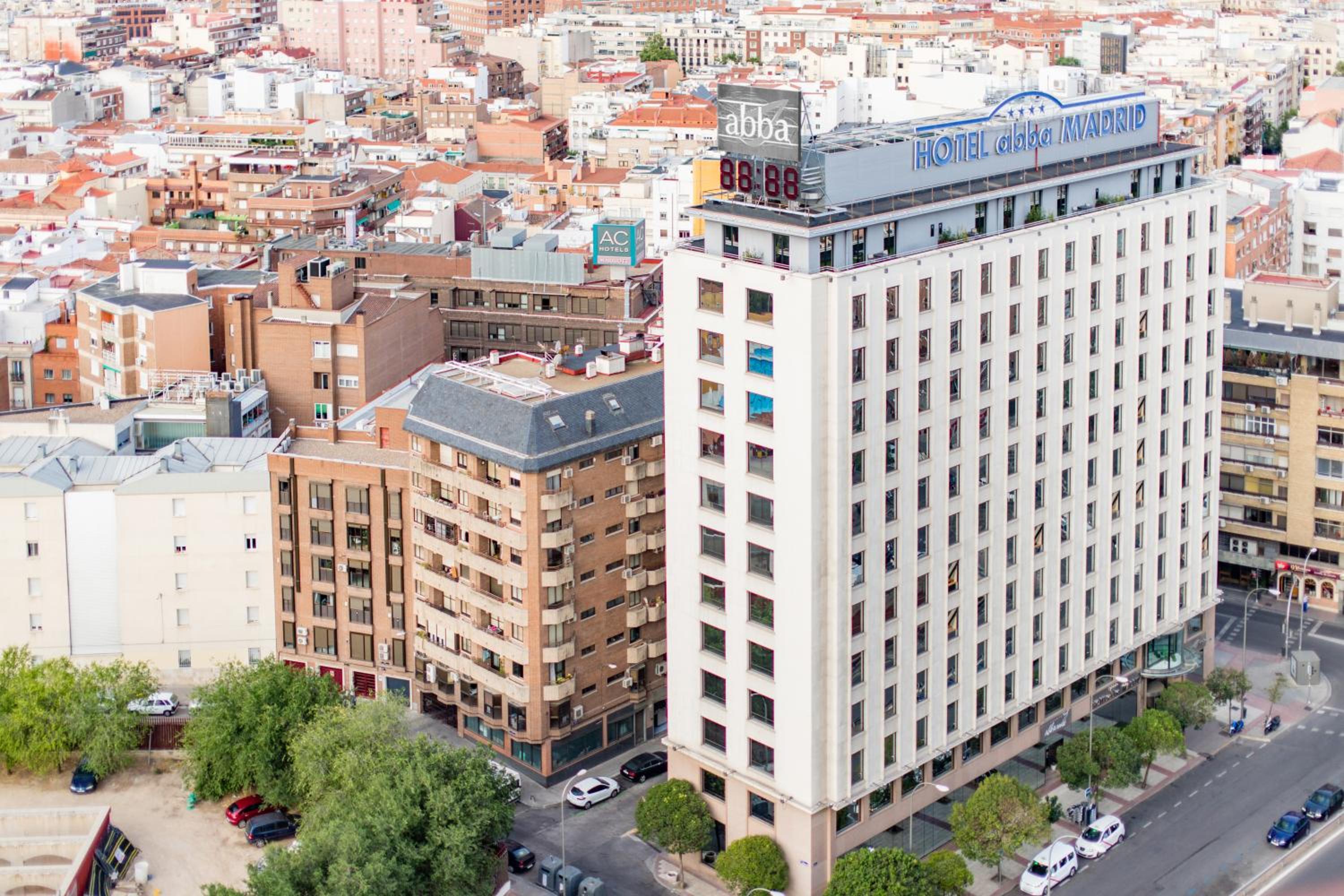 High-angle view of the Abba Madrid hotel tower surrounded by city apartment buildings under daylight.