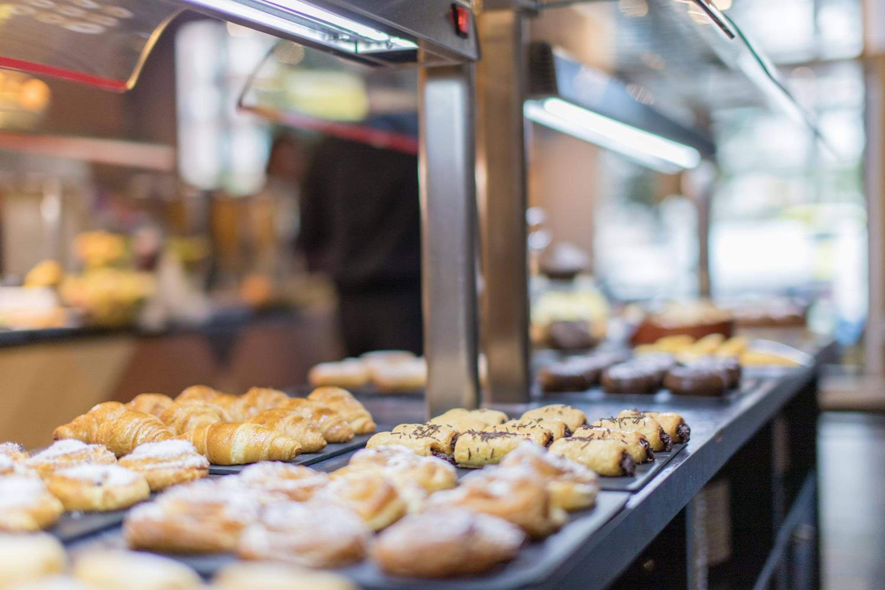 Buffet counter lined with trays of fresh croissants and filled pastries beneath overhead display lighting.