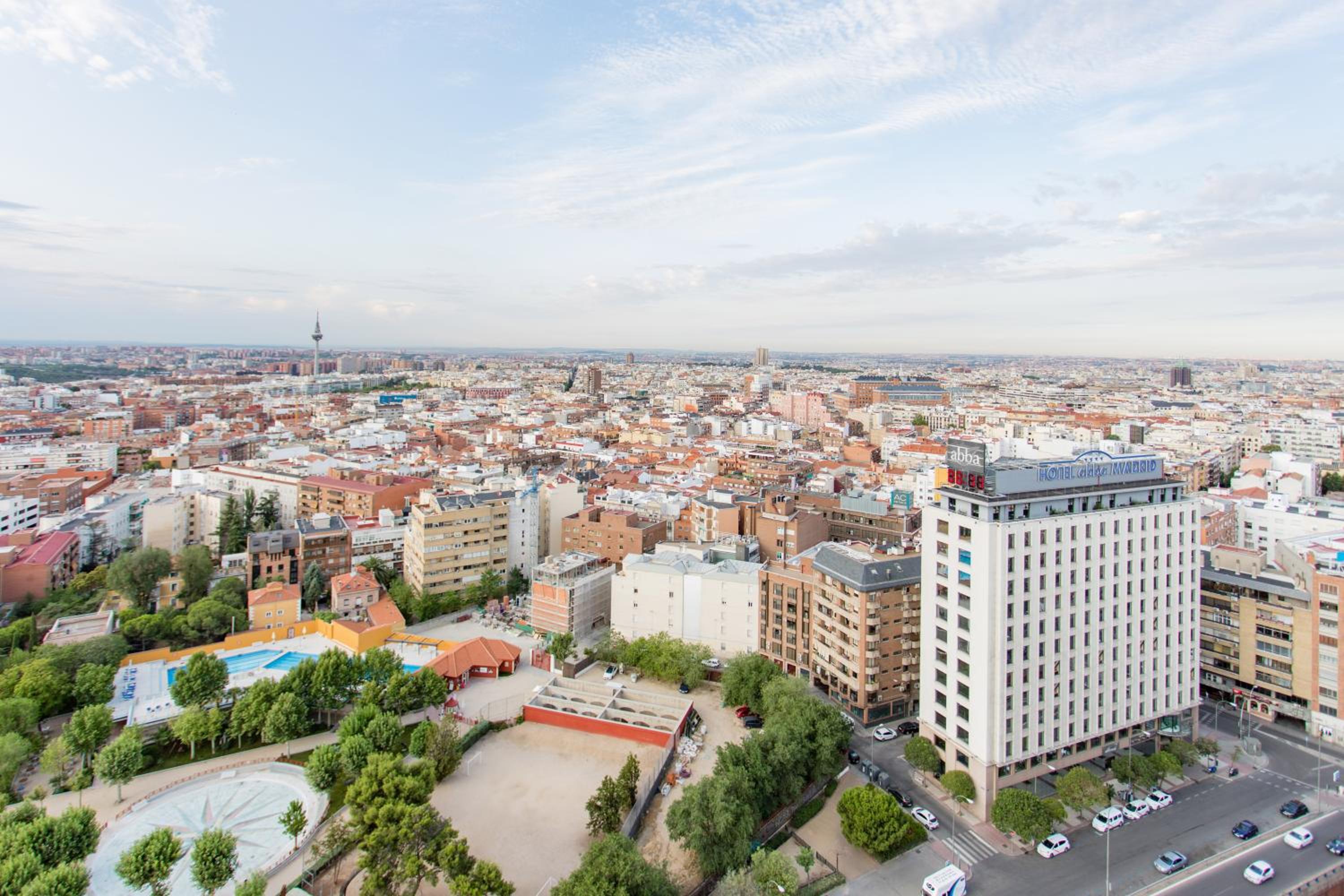 Panoramic elevated view over city rooftops, showing surrounding streets, residential blocks, and a green park.
