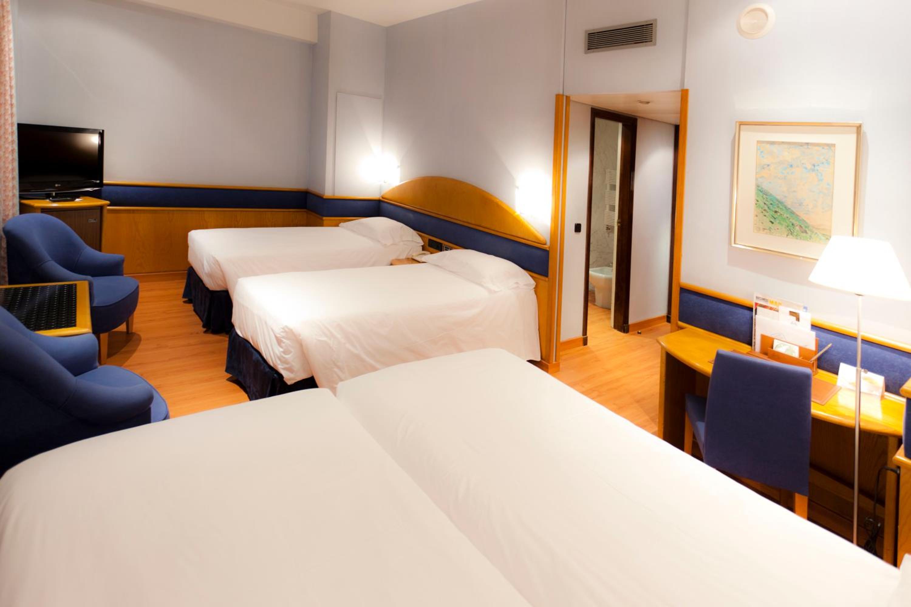 A guest room at Agumar Atocha with beds dressed in white linens, wood-trimmed blue walls, and a writing desk.