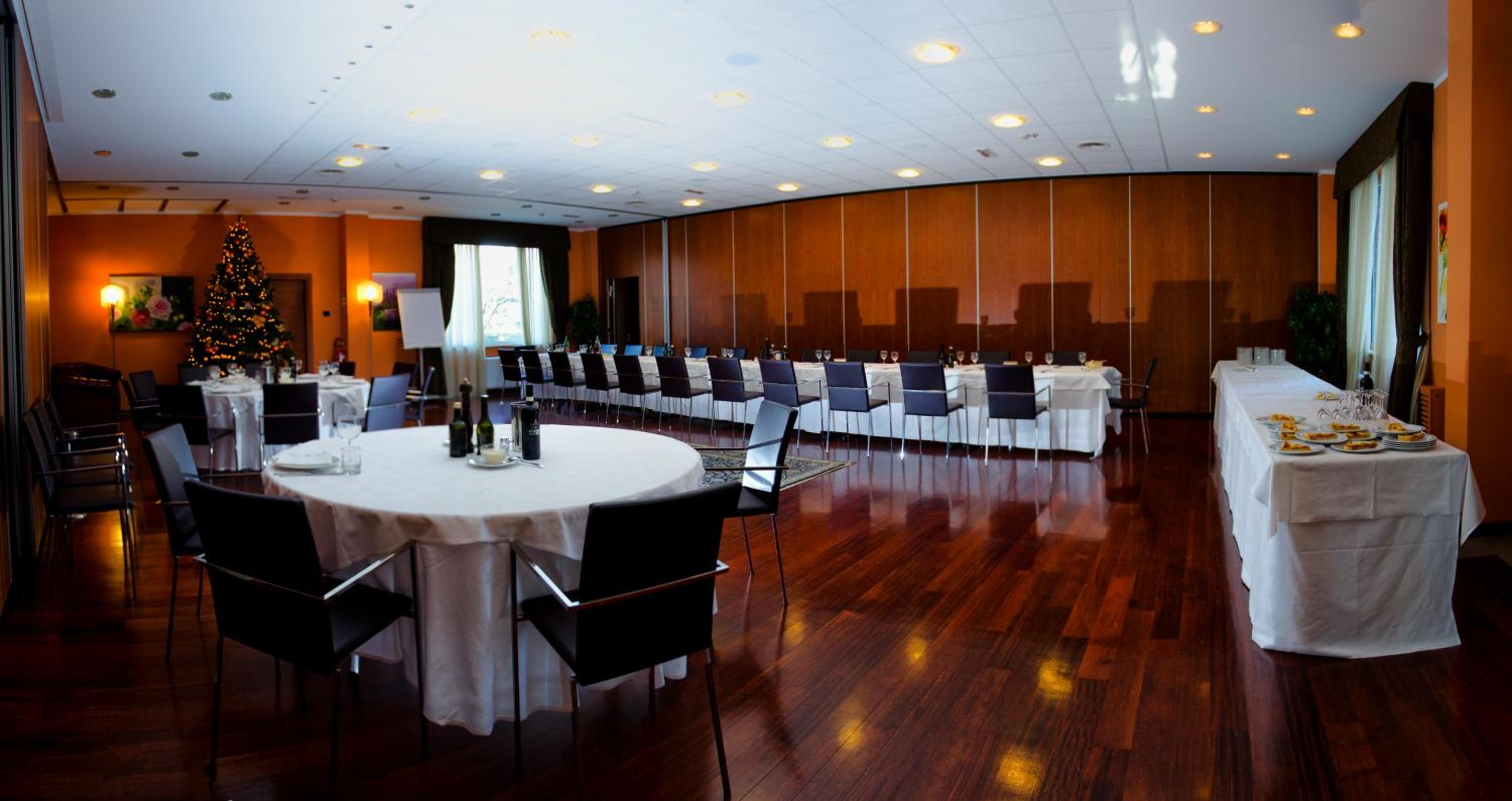 A banquet hall with polished wood flooring, paneled walls, set dining tables, and a decorated holiday tree.