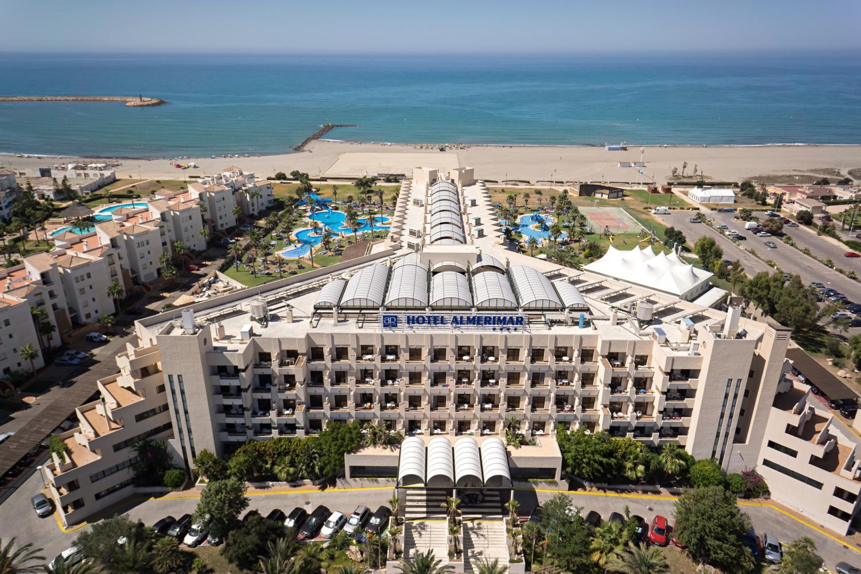 Aerial view of AR Almerimar hotel facade, swimming pools, and grounds beside a sandy beach and the sea.