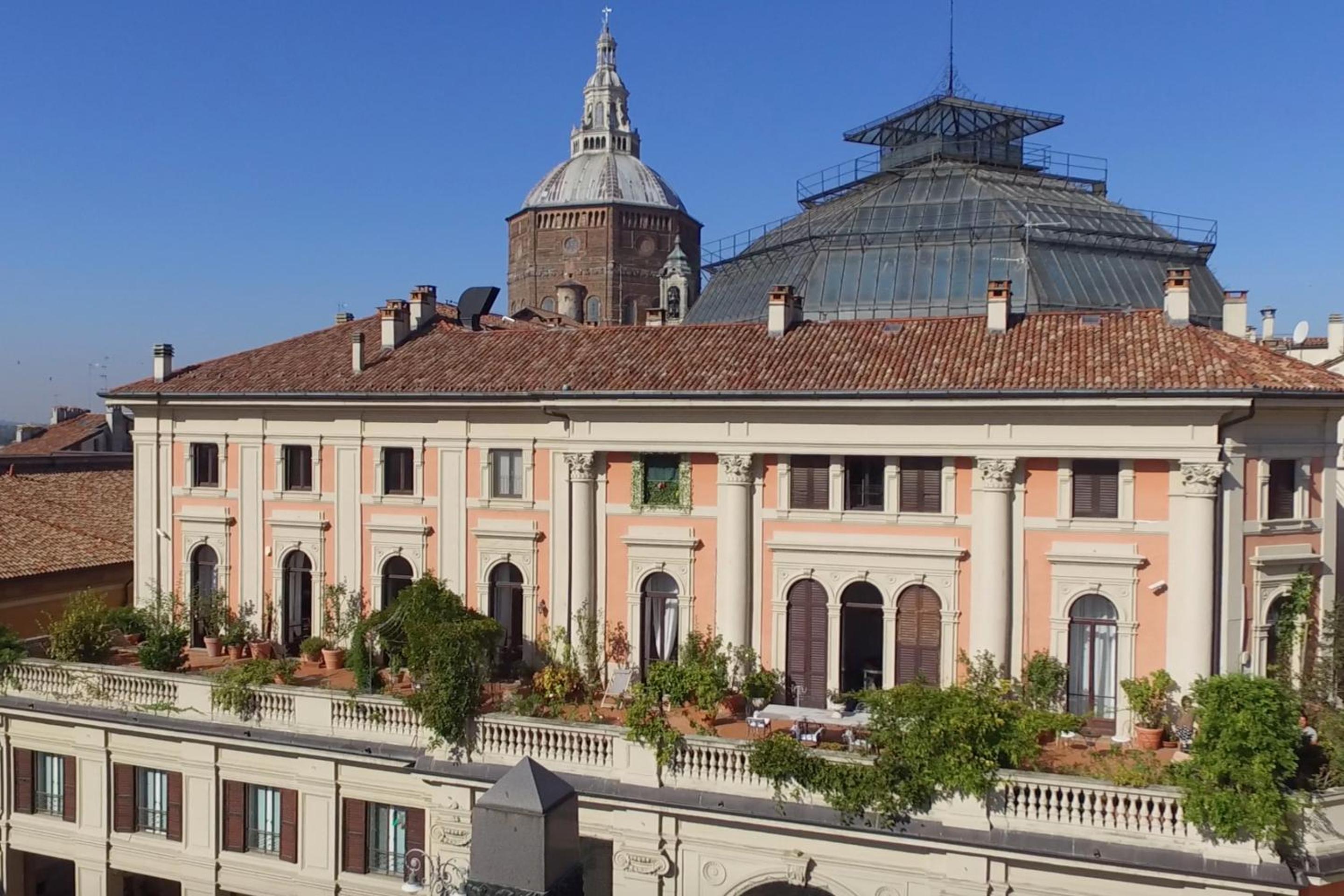 A rooftop terrace with potted plants along a classical facade, backed by a large dome and glass cupola.
