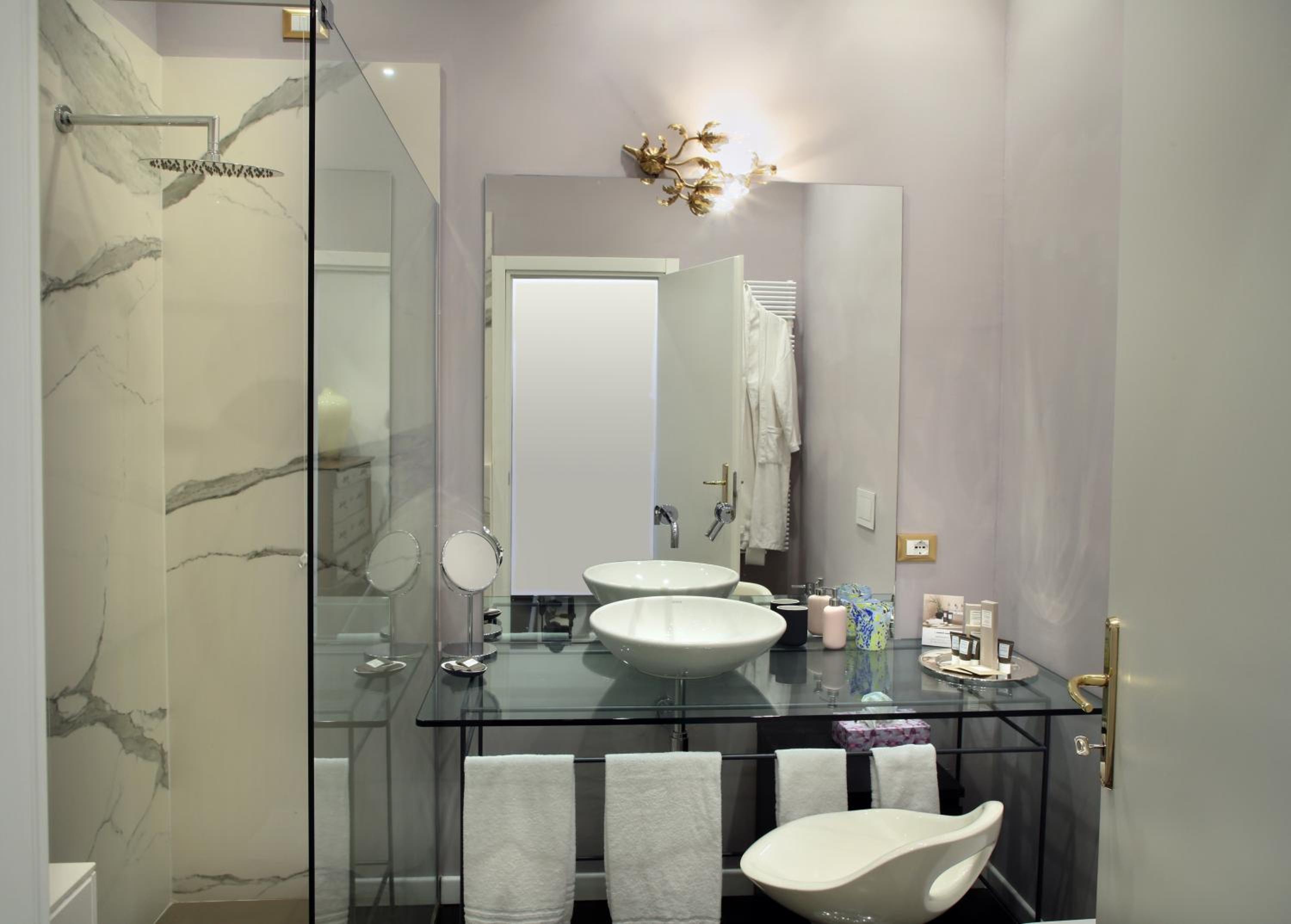 A bathroom with a marble-tiled shower, glass countertop with vessel basins, and a large mirror.